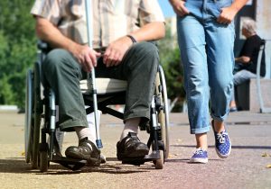 Rollstuhlfahrer mit Blindenstock und Betreuungskraft